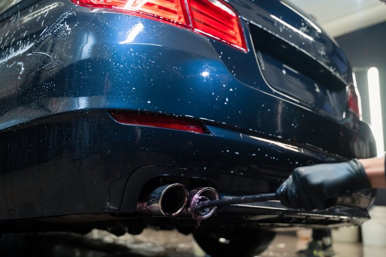 Detailing worker cleans exhaust pipe of car. Cleaning auto muffler with foam and brush.